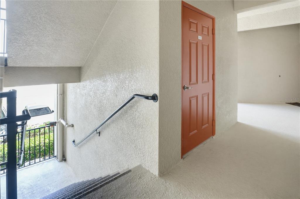 A staircase with a metal handrail leads to a landing with an orange entry door — 7005 RIVER HAMMOCK DRIVE UNIT 202, BRADENTON, FL