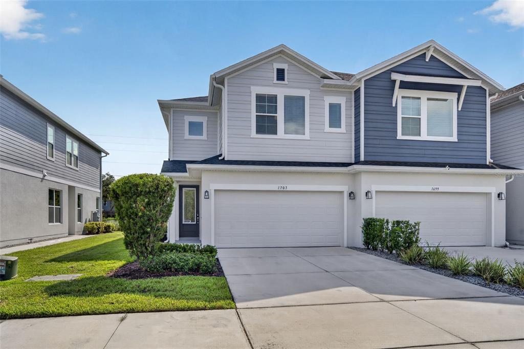 A two-story duplex house features light gray and blue siding with two attached garage doors — 1703 TERRAPIN ROAD, OCOEE, FL