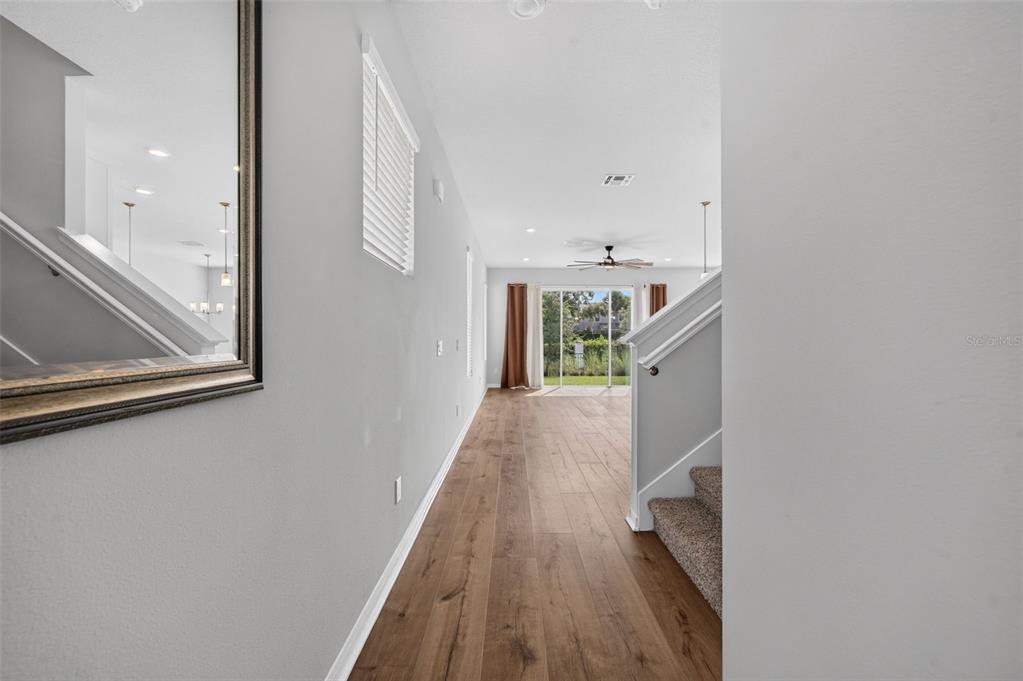 A hallway with wood-look flooring leads past a staircase toward a sliding glass door — 1703 TERRAPIN ROAD, OCOEE, FL
