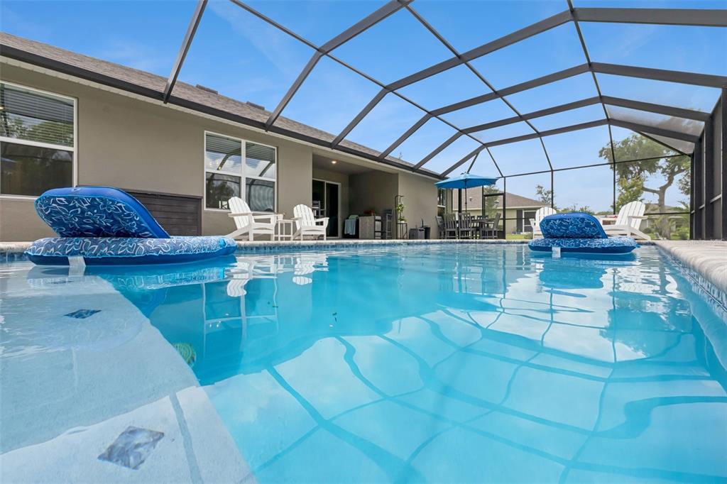 A swimming pool with two blue floats sits inside a screened-in patio area — 3093 ADRIAN DR, ORMOND BEACH, FL