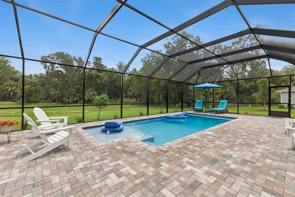 A screened-in pool patio features a paved deck, lounge chairs, and a view of trees — 3093 ADRIAN DR, ORMOND BEACH, FL
