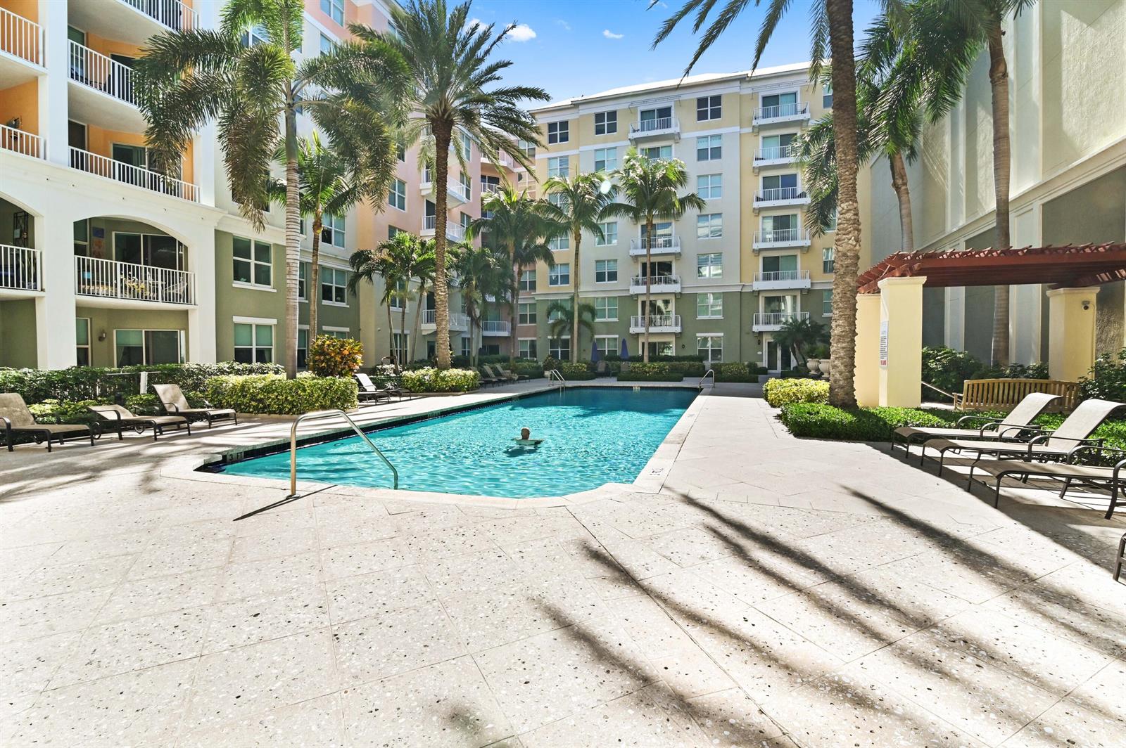A swimming pool is surrounded by lounge chairs, palm trees, and multi-story apartment buildings — 804 E Windward Way # 122, Lantana FL 33462, LANTANA, FL