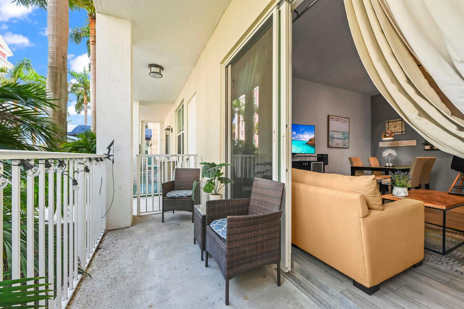 A balcony with wicker chairs overlooks a living room featuring a sofa and dining area — 804 E Windward Way # 122, Lantana FL 33462, LANTANA, FL