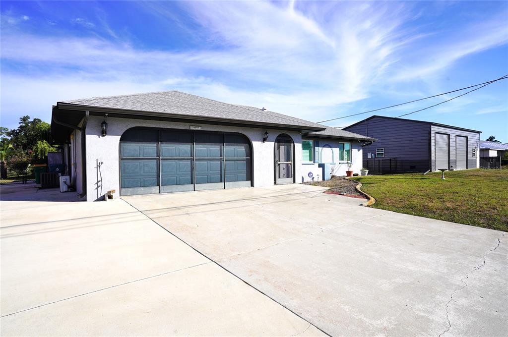 A single-story house with a large concrete driveway, a multi-panel garage door, and gray siding — 19891 MIDWAY BOULEVARD, PORT CHARLOTTE, FL