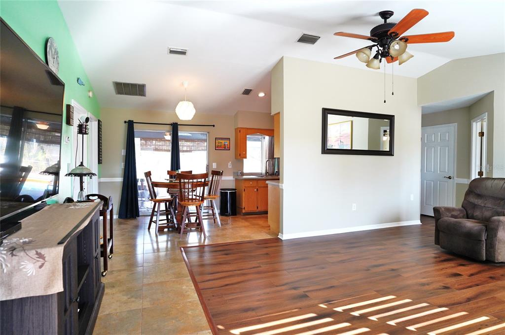 A living room with wood-look flooring transitions to a tiled dining area and kitchen — 19891 MIDWAY BOULEVARD, PORT CHARLOTTE, FL