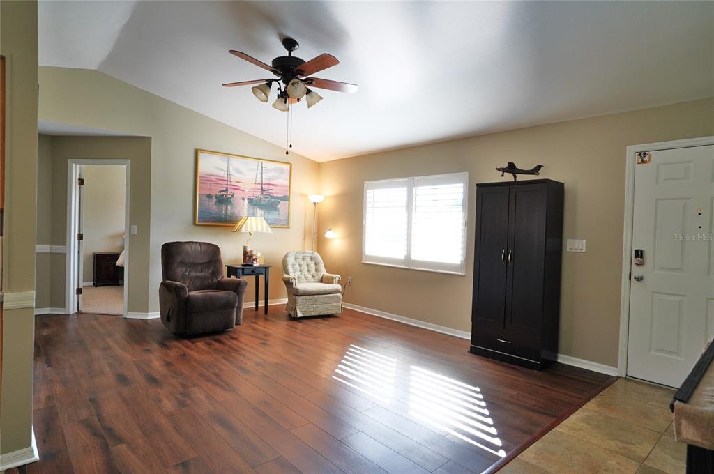 A living room features wood-look flooring, a ceiling fan, two armchairs, and a dark cabinet — 19891 MIDWAY BOULEVARD, PORT CHARLOTTE, FL