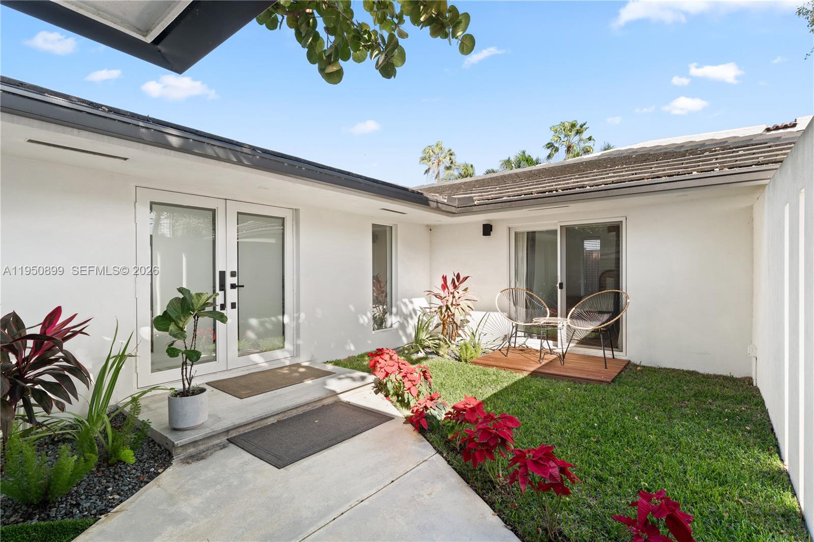 A white house exterior features a concrete walkway, a small wooden deck, and red plants — 1071 NE 83rd St, Miami FL 33138, MIAMI, FL