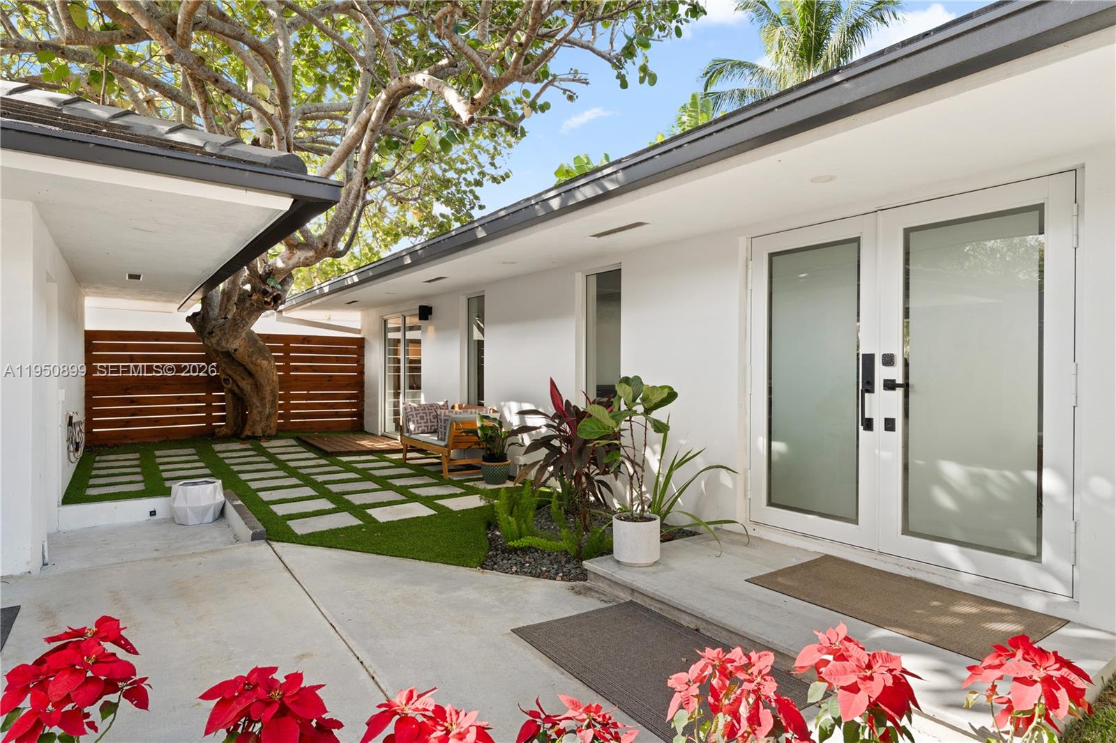 A modern home exterior features a white facade, glass double doors, and a paved courtyard — 1071 NE 83rd St, Miami FL 33138, MIAMI, FL