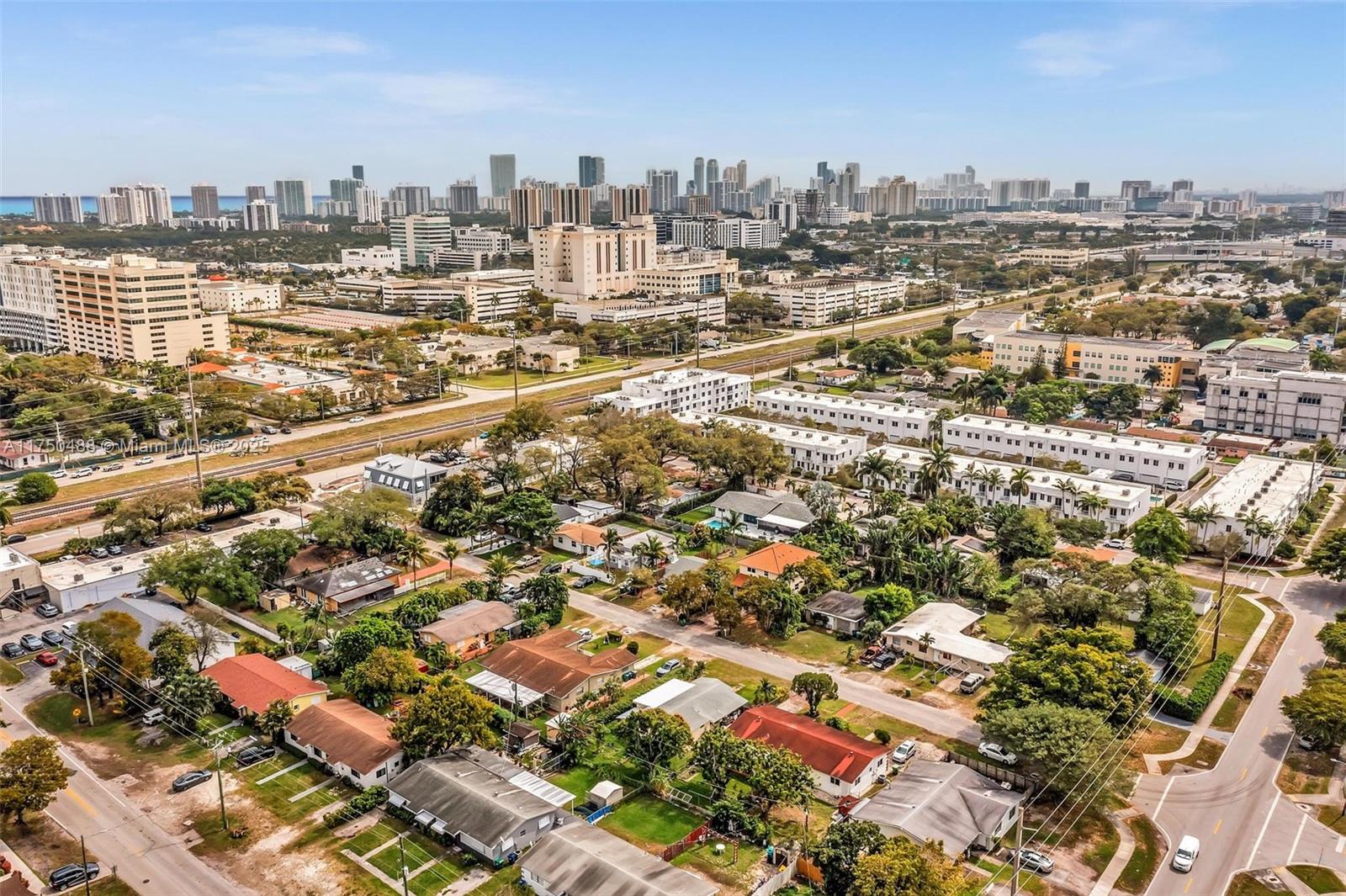 An aerial view shows a suburban neighborhood with houses, apartment complexes, and a distant city skyline — 2631 NE 214th St, Miami FL 33180, MIAMI, FL