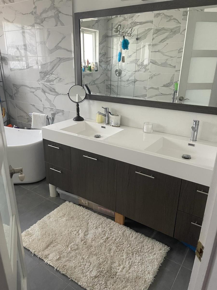 A bathroom features a double vanity with dark wood cabinets, marble-look wall tiles, and a tub — 6807 Via Regina # 1, Boca Raton FL 33433, BOCA RATON, FL