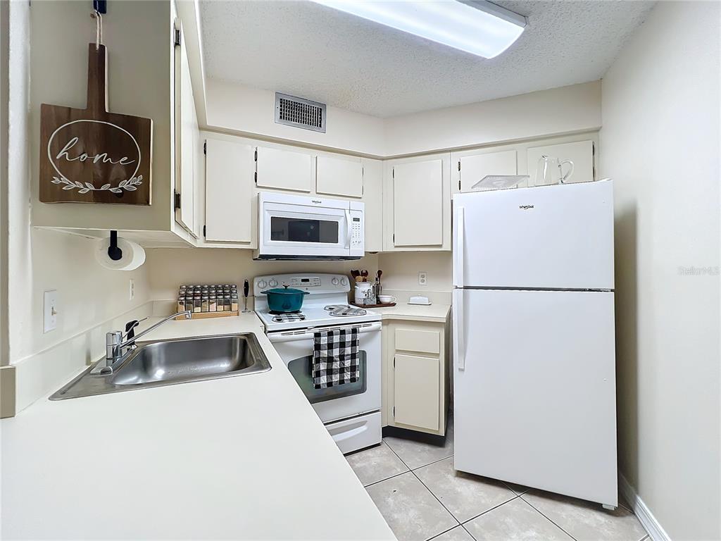 A kitchen features white cabinetry, white appliances, a stainless steel sink, and tiled flooring — 3642 SOUTHPOINTE DRIVE UNIT L6, ORLANDO, FL