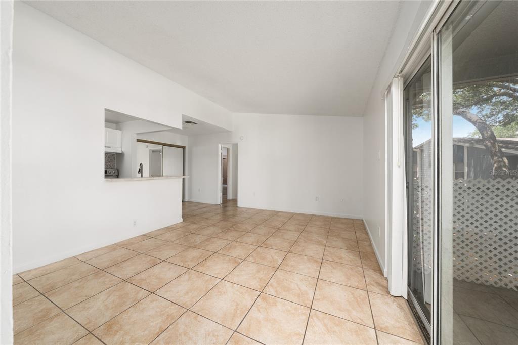 An open living area features beige tile flooring, white walls, and a sliding glass door — 3849 BAY CLUB CIRCLE UNIT 204, KISSIMMEE, FL