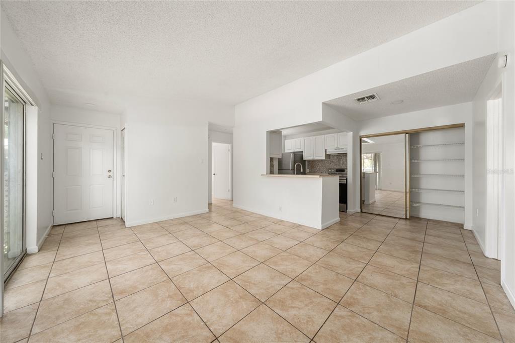 An open-concept living area features beige tile flooring, white walls, and a pass-through kitchen — 3849 BAY CLUB CIRCLE UNIT 204, KISSIMMEE, FL