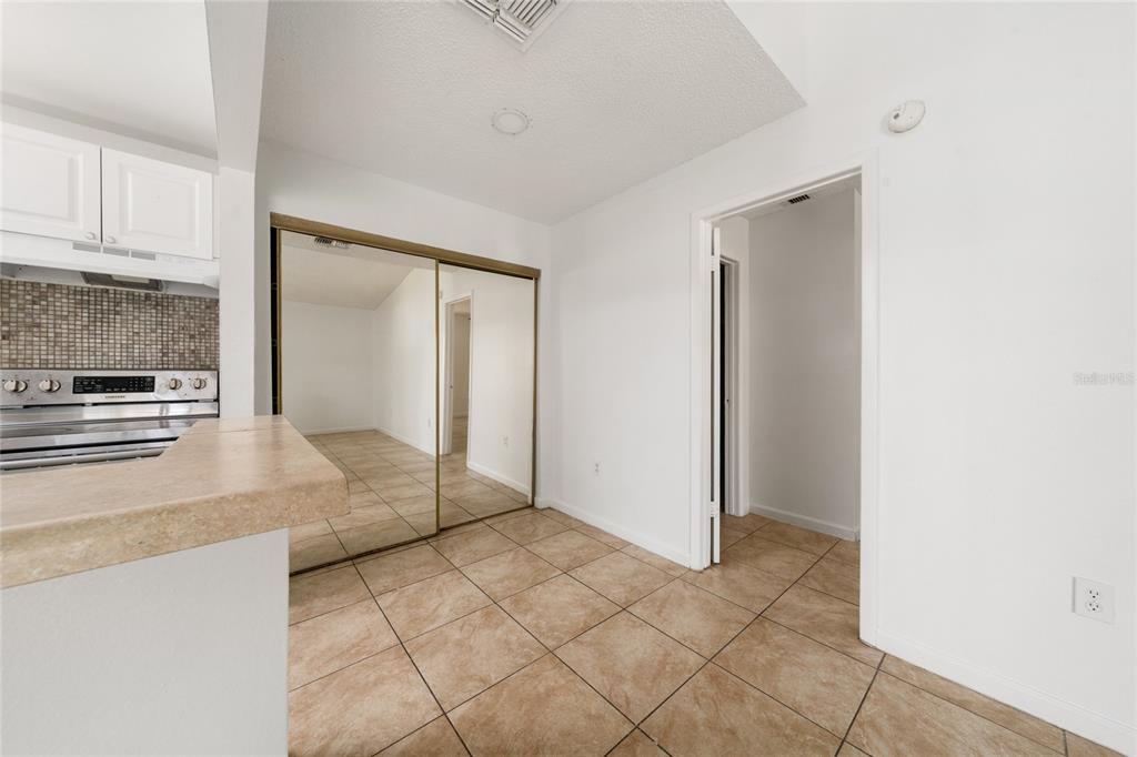 A kitchen area with tiled floors, mirrored closet doors, and a doorway leading to a hallway — 3849 BAY CLUB CIRCLE UNIT 204, KISSIMMEE, FL