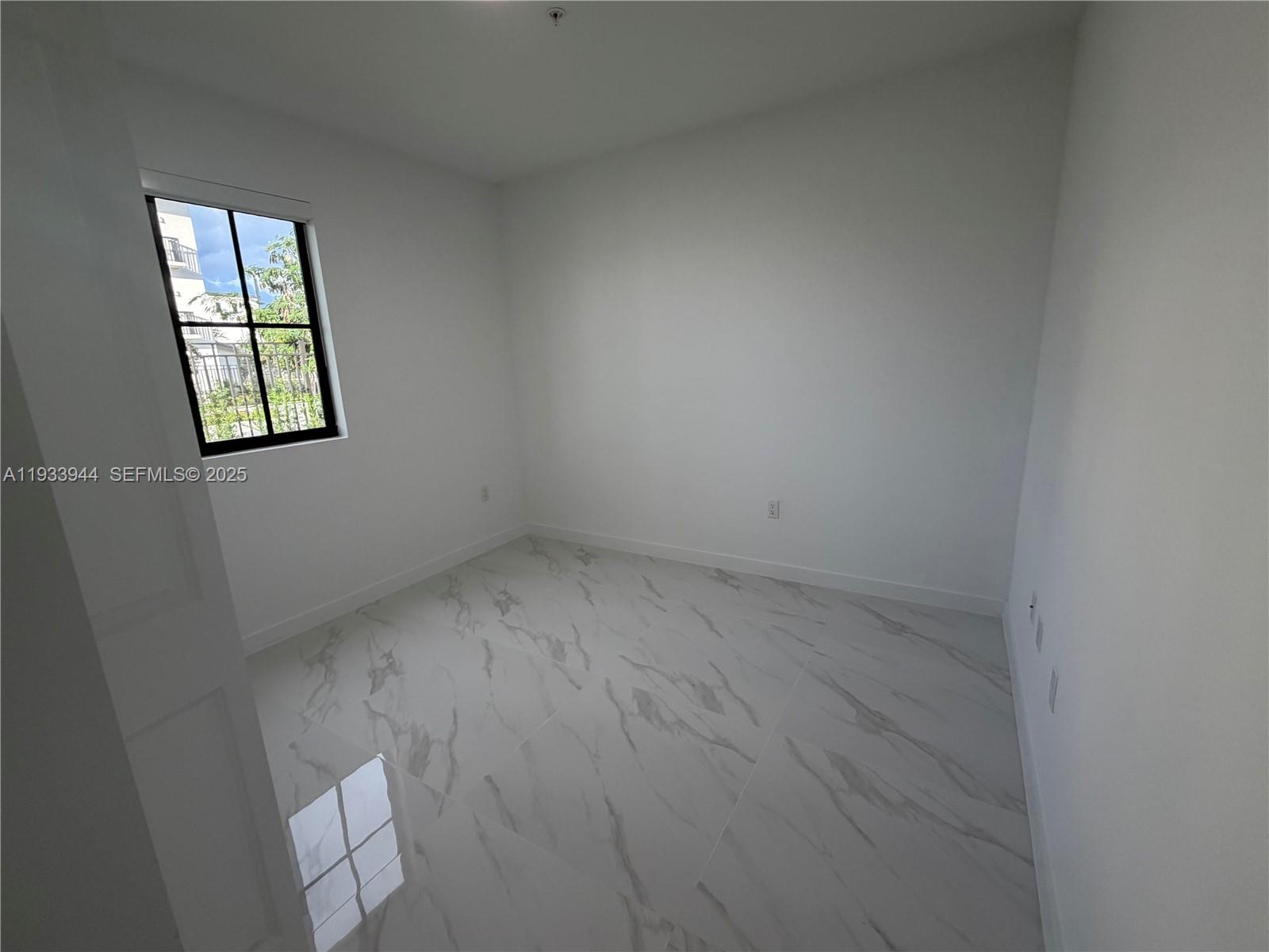 An empty room features white walls, large marble-patterned floor tiles, and a window with black frames — 2306 E 4th ave # 303, Hialeah FL 33013, HIALEAH, FL