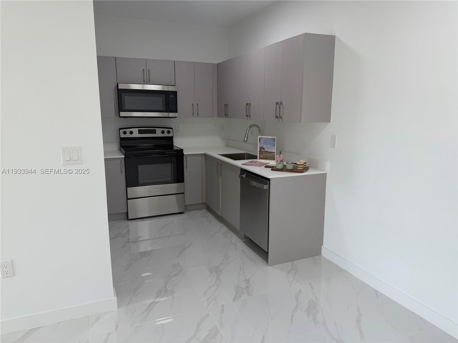 A modern kitchen features gray cabinets, stainless steel appliances, and white marble-patterned tile flooring — 2306 E 4th ave # 303, Hialeah FL 33013, HIALEAH, FL