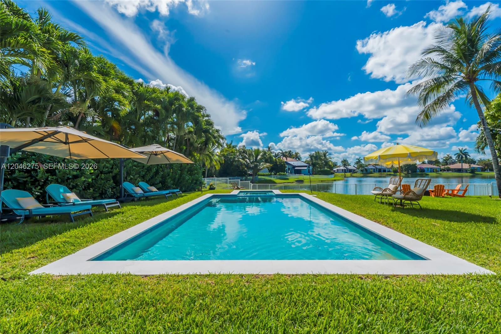 A rectangular swimming pool sits in a grassy backyard overlooking a lake with palm trees — 4135 SW 186th Way, Miramar FL 33029, MIRAMAR, FL