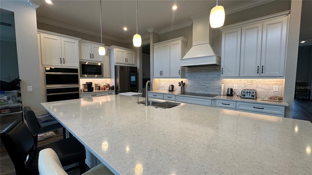A modern kitchen features a large quartz island, white cabinetry, and stainless steel appliances — 6875 BROGLIE STREET, ORLANDO, FL