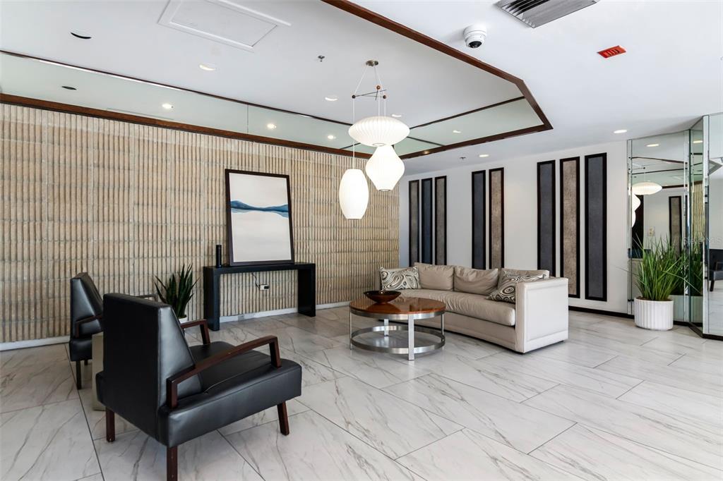 A modern lobby features a beige sofa, black armchairs, a coffee table, and pendant lighting — 1660 GULF BOULEVARD UNIT 407, CLEARWATER BEACH, FL
