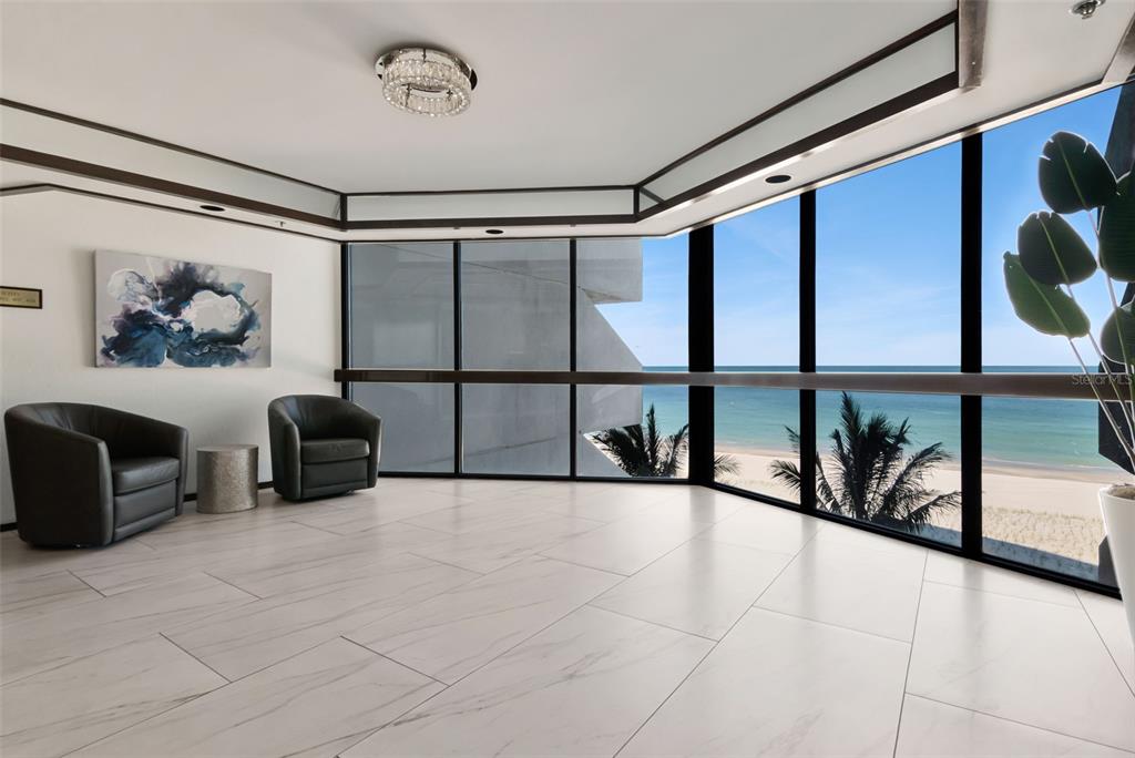 A modern room with white tile floors, two leather chairs, and floor-to-ceiling ocean view windows — 1660 GULF BOULEVARD UNIT 407, CLEARWATER BEACH, FL