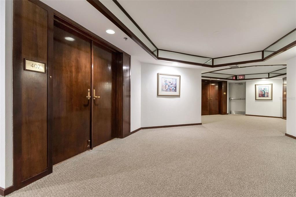 A carpeted hallway features dark wood double doors marked 407 and framed wall art — 1660 GULF BOULEVARD UNIT 407, CLEARWATER BEACH, FL