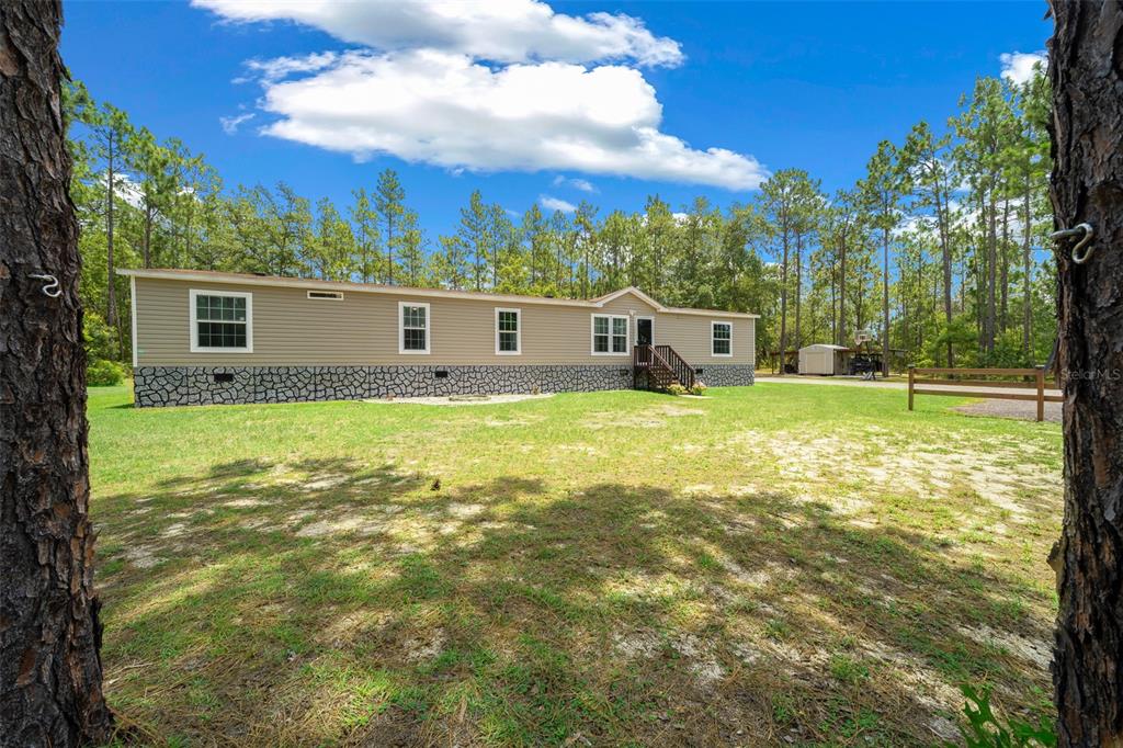 A tan manufactured home with a stone-patterned skirting sits on a grassy, wooded lot — 105 BUCK RUN TRAIL, HAWTHORNE, FL