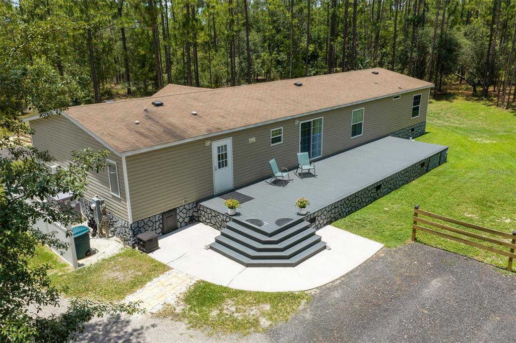An elevated view of a manufactured home with a large deck and stone-patterned skirting — 105 BUCK RUN TRAIL, HAWTHORNE, FL