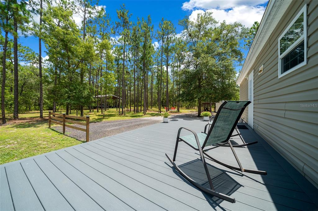 A gray wooden deck with rocking chairs overlooks a wooded yard with a gravel driveway — 105 BUCK RUN TRAIL, HAWTHORNE, FL