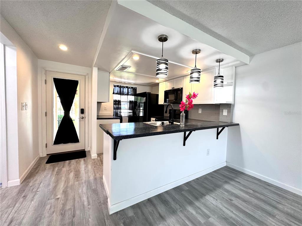 A kitchen features a black countertop breakfast bar, white cabinetry, and three hanging pendant lights — 4445 RUSTIC DRIVE, NEW PORT RICHEY, FL