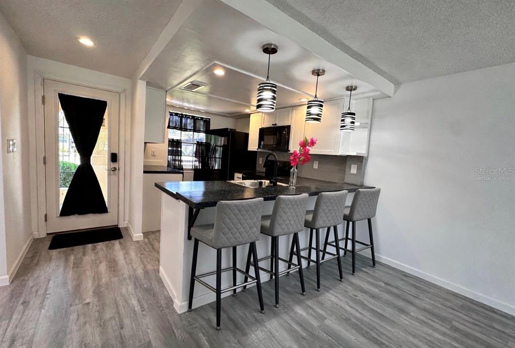A kitchen features a breakfast bar with four gray stools, white cabinets, and pendant lighting — 4445 RUSTIC DRIVE, NEW PORT RICHEY, FL