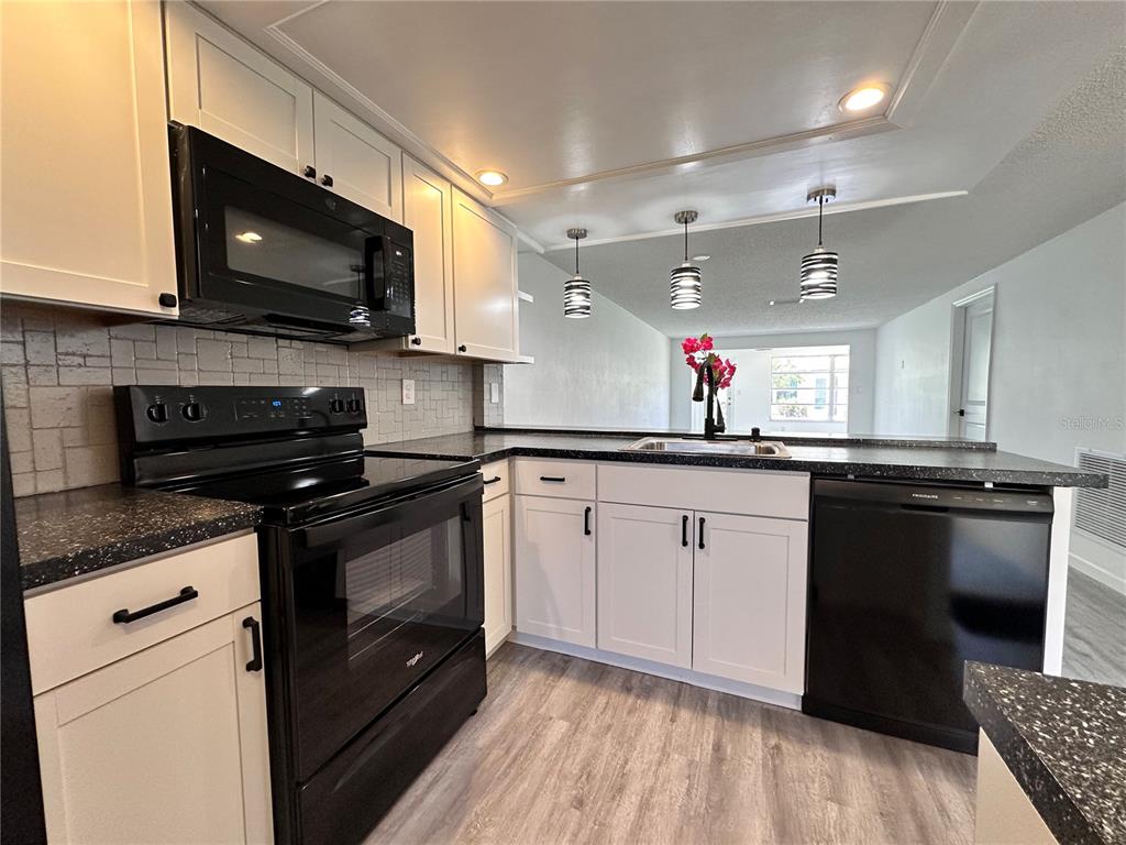 A kitchen with white cabinets, black appliances, and dark speckled countertops — 4445 RUSTIC DRIVE, NEW PORT RICHEY, FL