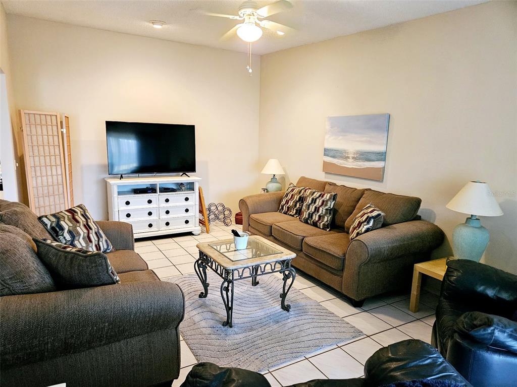 A living room features brown sofas, a glass-top coffee table, and a television on a stand — 4107 41ST STREET W, BRADENTON, FL