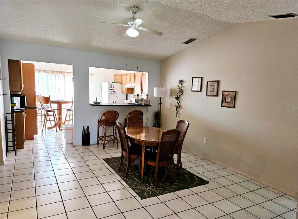 A dining area with a round wooden table, chairs, and a pass-through to the kitchen — 4107 41ST STREET W, BRADENTON, FL