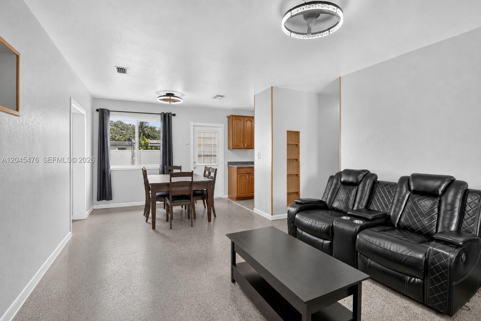This living and dining area features gray walls, speckled flooring, and a black leather sofa — 7331 Garfield St, Hollywood FL 33024, HOLLYWOOD, FL