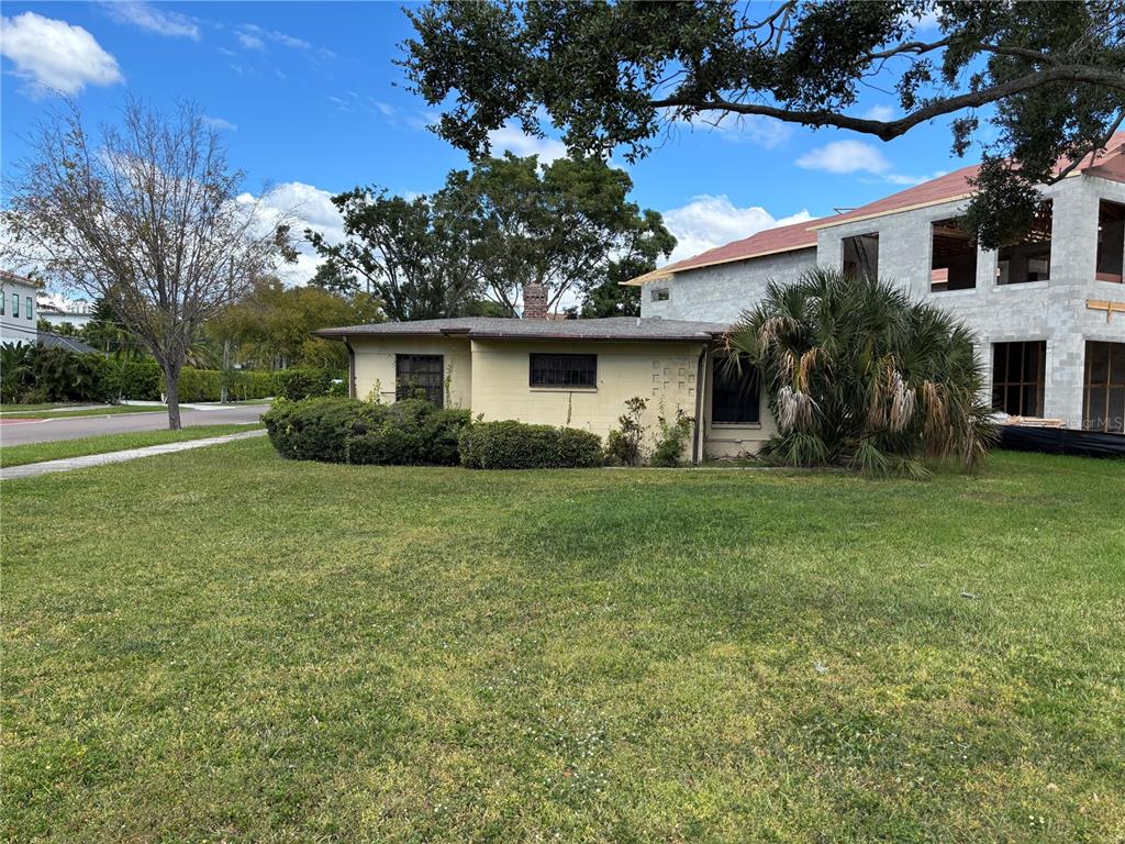 A single-story yellow house sits next to a large, unfinished multi-story concrete building — 61 ADALIA AVENUE, TAMPA, FL