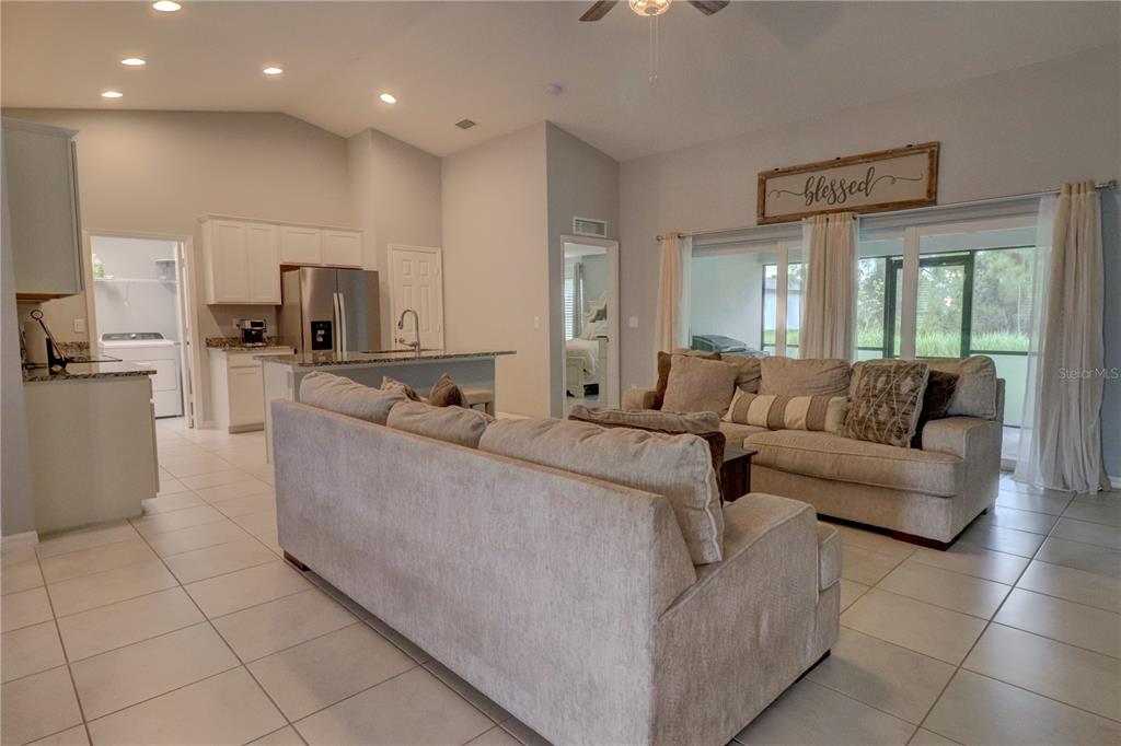 An open-concept living room and kitchen with tile floors, neutral furniture, and sliding glass doors — 2713 EMBASSY ROAD, NORTH PORT, FL