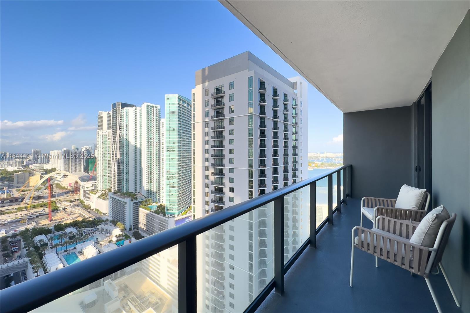 A high-rise balcony features two chairs overlooking a dense urban skyline and a body of water — 601 NE 1st Av # 4402, Miami FL 33132, MIAMI, FL