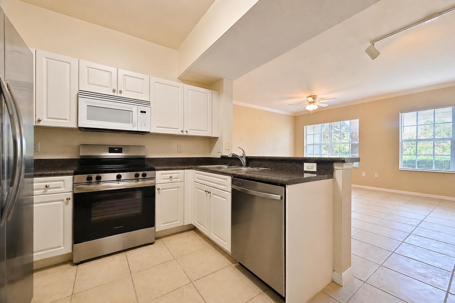 A kitchen with white cabinets, stainless steel appliances, and dark countertops opens to a living area — 356 SE Rogers Court, Stuart FL 34994, STUART, FL