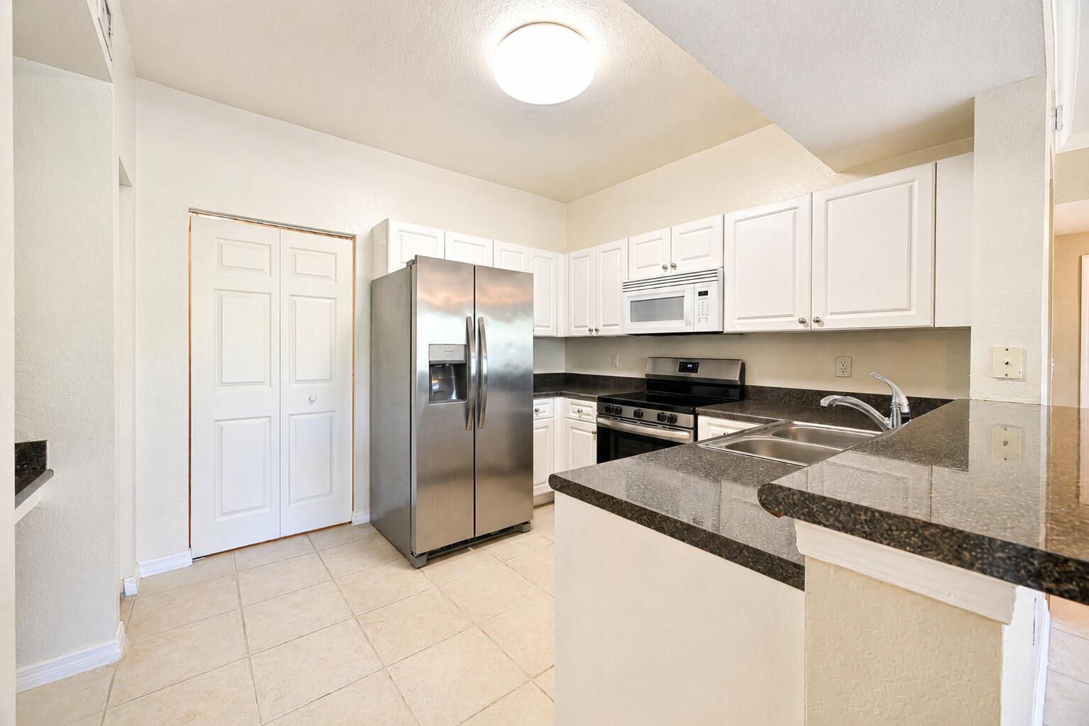 A kitchen features white cabinets, stainless steel appliances, and dark granite countertops — 356 SE Rogers Court, Stuart FL 34994, STUART, FL