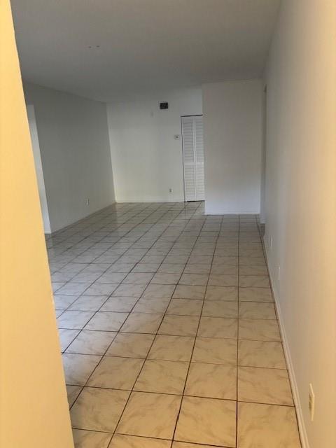 An empty room with light-colored tile flooring and white walls leads to a closet door — 501 Gardens Drive # 101, Pompano Beach FL 33069, POMPANO BEACH, FL
