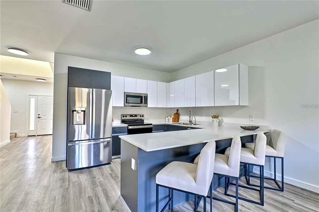 A modern kitchen features white upper cabinets, dark lower cabinets, stainless steel appliances, and a peninsula — 1589 NW 29TH ROAD UNIT 7, GAINESVILLE, FL