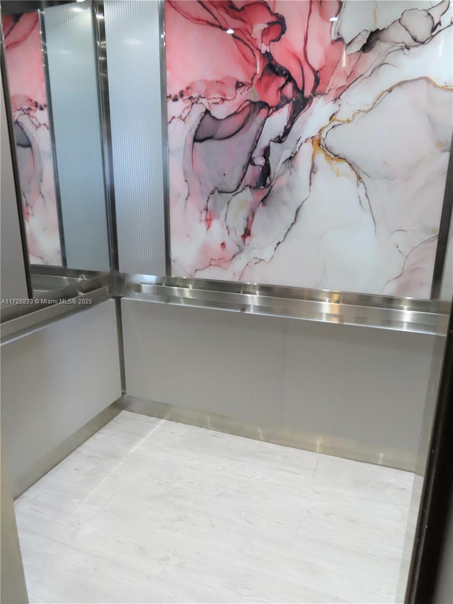 An elevator interior features a pink and white marble-patterned wall panel and metallic trim — 5701 Collins Ave # 1011, Miami Beach FL 33140, MIAMI BEACH, FL