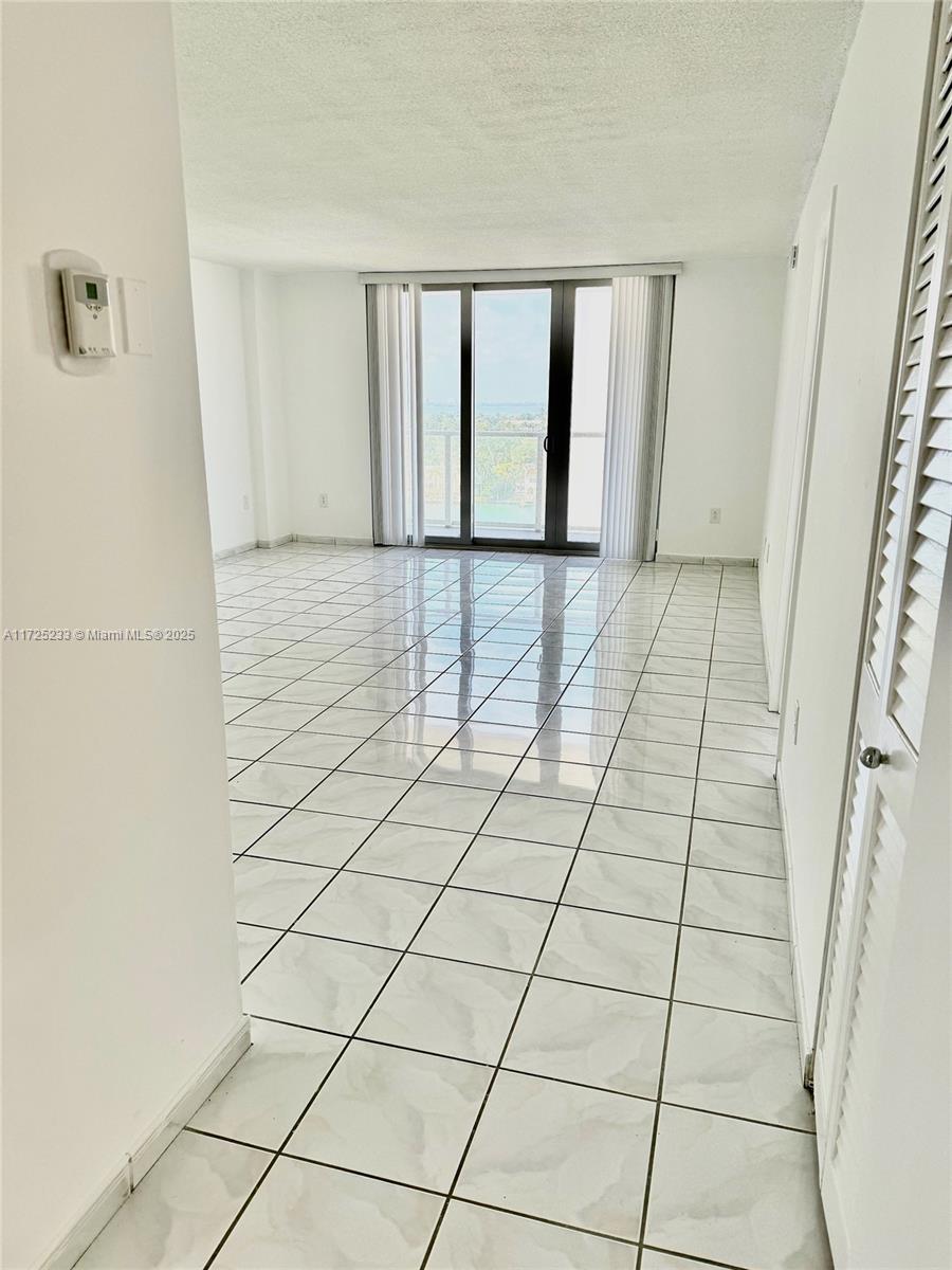 An empty room features white tiled floors, white walls, and a sliding glass balcony door — 5701 Collins Ave # 1011, Miami Beach FL 33140, MIAMI BEACH, FL