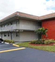 A two-story building features a second-floor balcony, gray stucco walls, and a red accent wall — 609 S State Road 7 # 1E, Margate FL 33068, MARGATE, FL