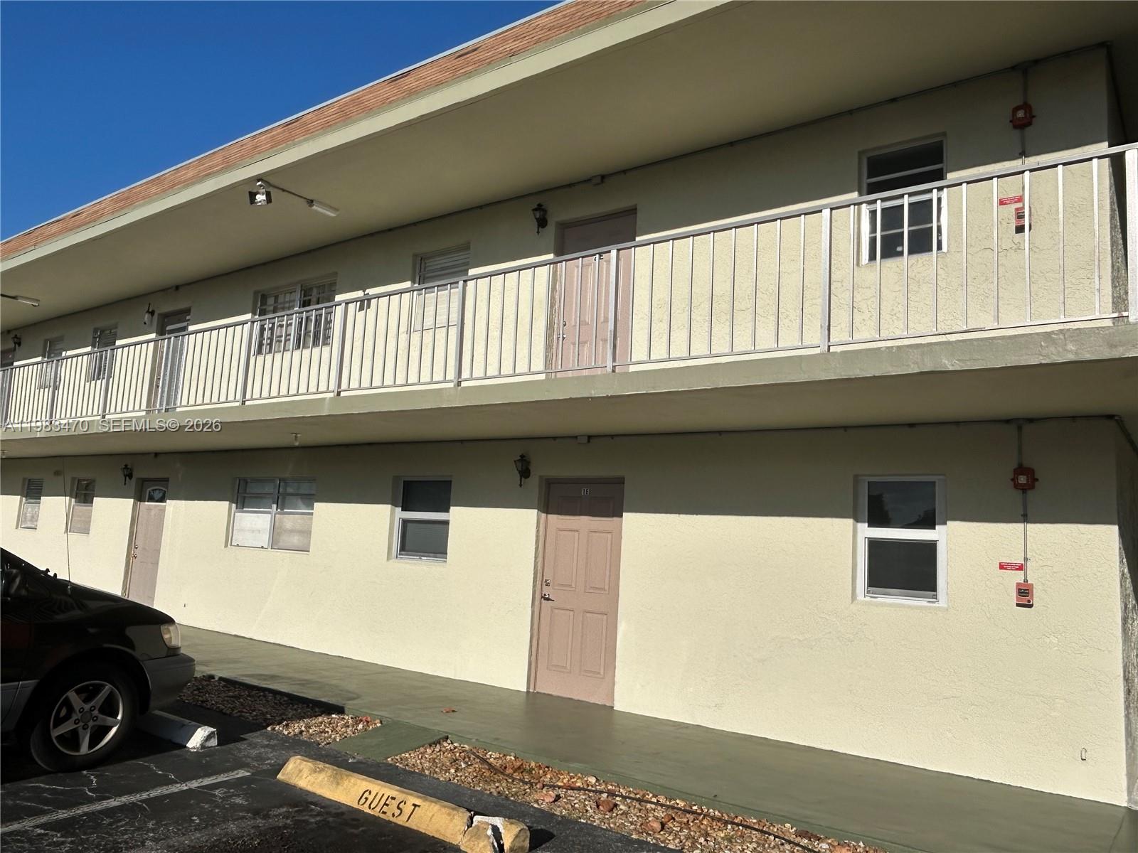 A two-story apartment building exterior features a concrete walkway, metal railings, and tan doors — 609 S State Road 7 # 1E, Margate FL 33068, MARGATE, FL