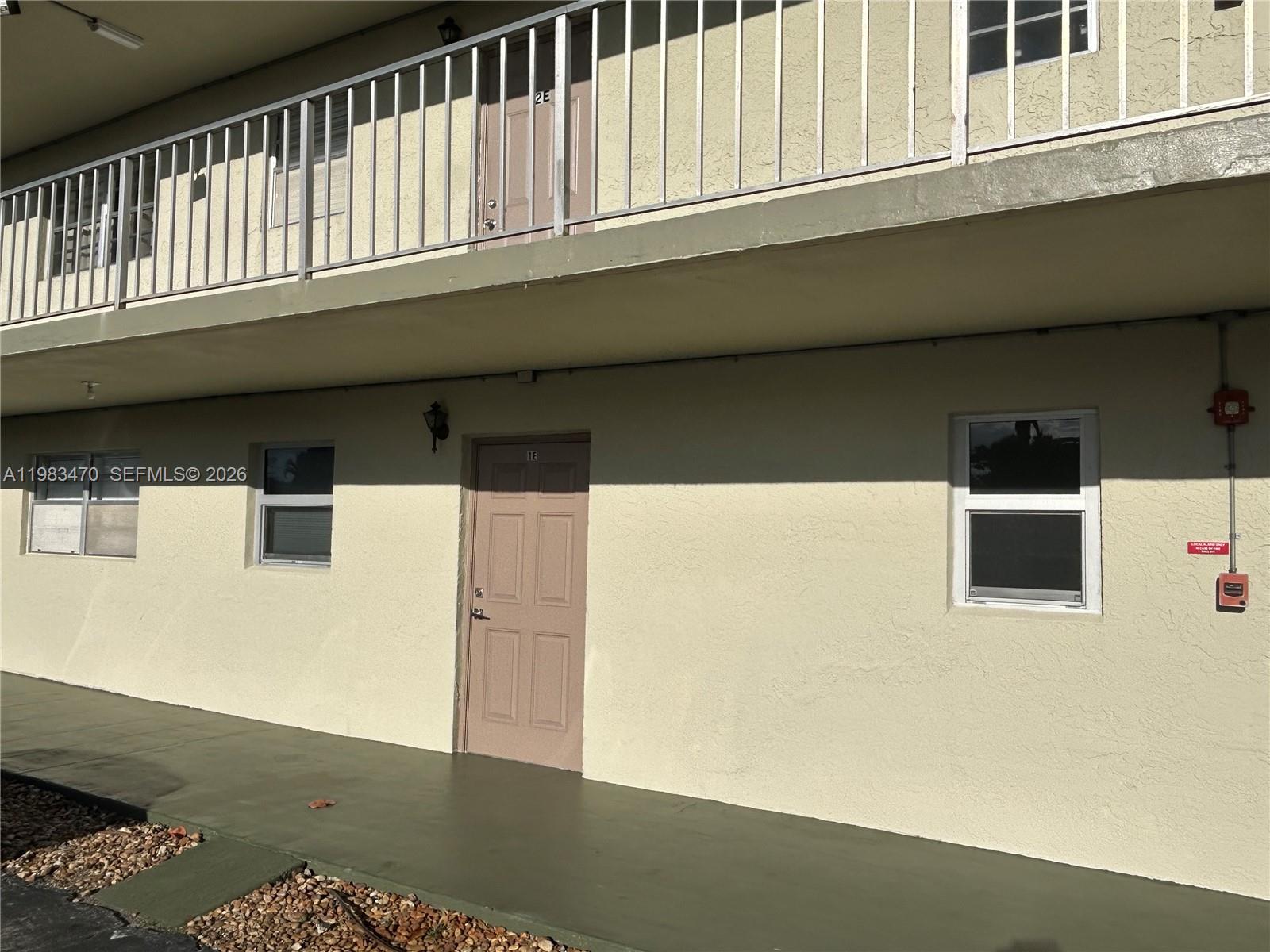 The exterior of a two-story apartment building features a ground-level unit with a brown door — 609 S State Road 7 # 1E, Margate FL 33068, MARGATE, FL