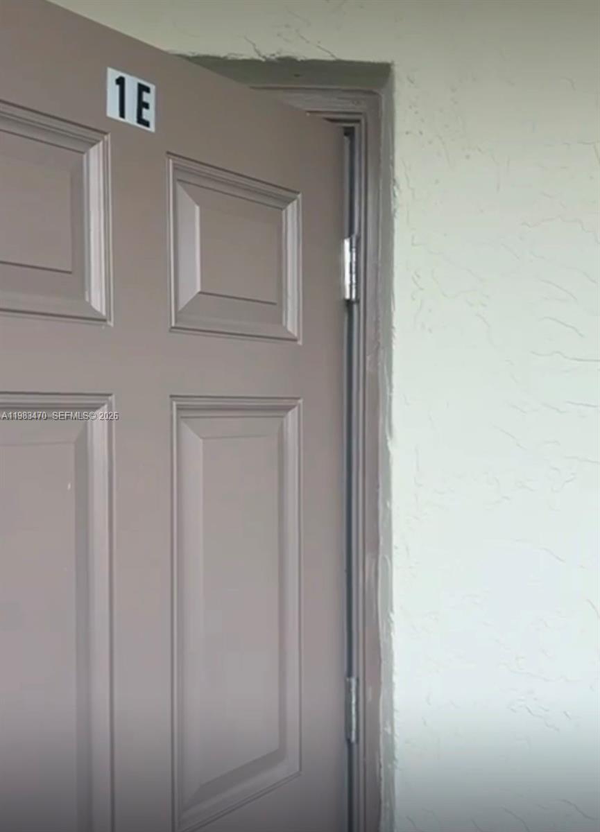 A beige door labeled 1E is slightly ajar against a textured off-white wall — 609 S State Road 7 # 1E, Margate FL 33068, MARGATE, FL