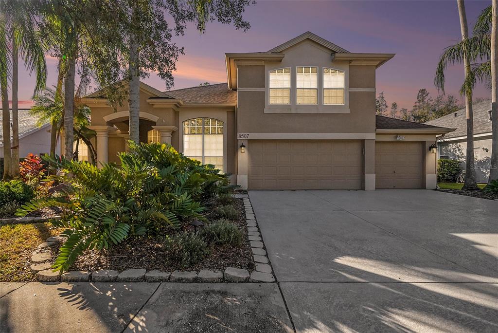 A two-story suburban house features a tan stucco exterior, a three-car garage, and landscaping — 8507 PORTAGE AVENUE, TAMPA, FL