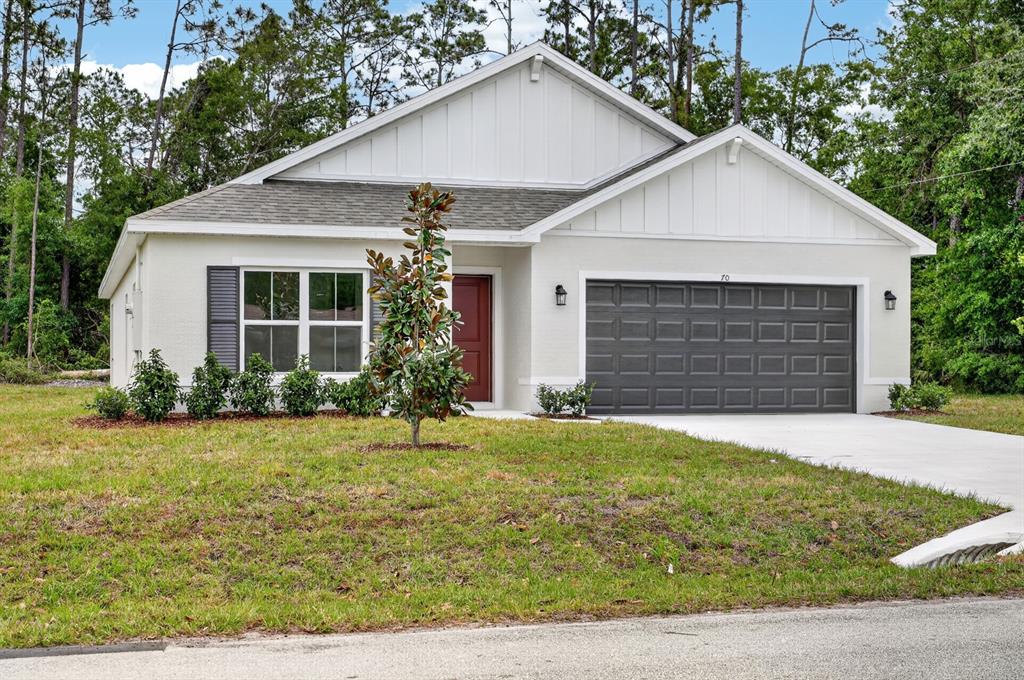 A single-story house with a white exterior, dark garage door, and a red front door — 70 WELLWATER DRIVE, PALM COAST, FL