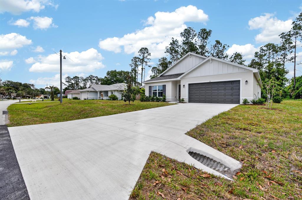 A modern, single-story house with a white exterior, dark garage door, and a concrete driveway — 70 WELLWATER DRIVE, PALM COAST, FL